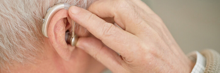 Close-up shot of an elderly person's ear wearing and adjusting a hearing aid device. Image...
