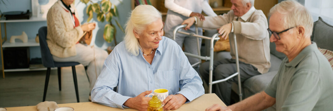 Elderly people engaged in conversation and activities in communal area of nursing home, showing warm interactions and caregiver assistance