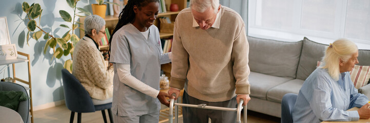 Senior man using walker being assisted by nurse in elderly care facility