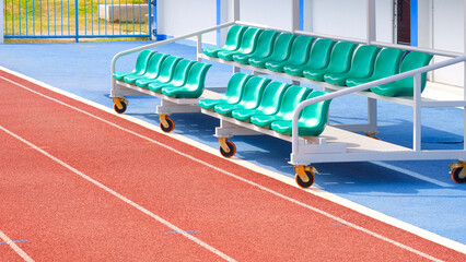 Reserve and coaching staff bench on rubber floor with red synthetic running tracks in outdoor...