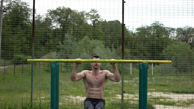 Hardy shirtless sportsman doing exercises on parallel bars at nature. Strong and muscular man working out at sports ground. Young athletic guy exercising outdoor. Concept of active healthy lifestyle