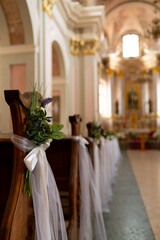 The benches in the church are beautifully decorated with white ribbons and flowers for the wedding ceremony