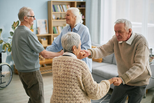 Group of elderly individuals engaging in conversation and smiling, while holding hands and enjoying each other's company at a community center event