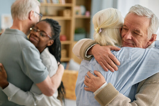 Elderly couple warmly embracing younger family members in cozy living room with soft lighting and decor creating comforting and affectionate atmosphere showcasing family bonds