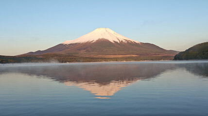 Snow-capped Fuji perfectly mirrored in obsidian lake, creating symmetrical majesty under crystal-clear blue sky.