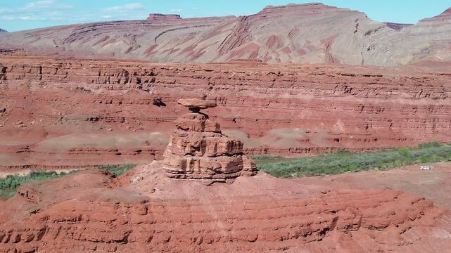 Mexican Hat rock formation in southern Utah. Low angle rotating pan shot that shows the formation, river below, and Raplee Ridge formation in the background.