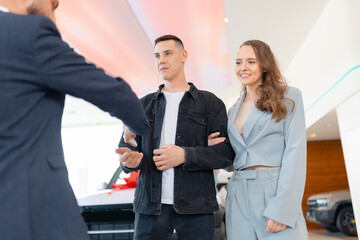 Car dealership business concept. Beautiful couple is holding key of their new car from salesman