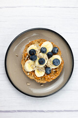 Sandwich with peanut butter, banana, blueberry and seeds on white table. Top view
