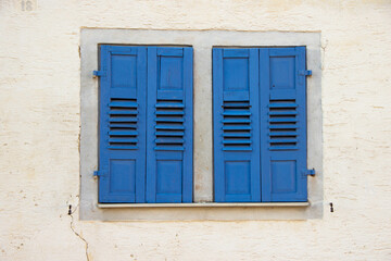 Closed wooden window with classic blue shutters in traditional European style, set in a rustic building facade.