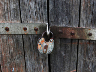 Close-up of an antique rusted padlock locking a worn wooden door, textured metal and peeling paint