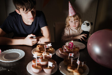 Siblings celebrating a birthday with cupcakes, decorations, and a plush toy