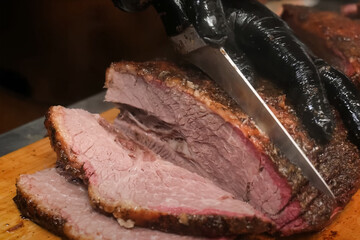 Sliced smoked brisket being carved with a sharp knife on a wooden board, showing juicy interior and bark texture, with gloved hand guiding the cut

