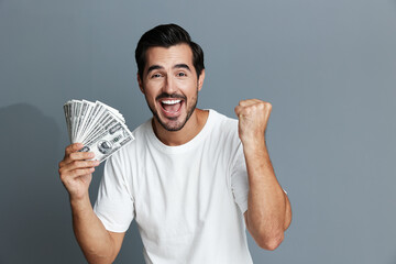 Excited cheerful young man celebrating success, holding cash money stacks in hand, isolated on solid gray background. Business lifestyle concept.