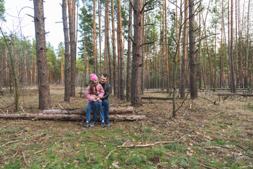 A father and daughter with skateboards are relaxing on a log in the forest.