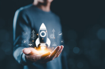 Startup Launch and Business Development Concept. Hand presenting glowing rocket icon with business...
