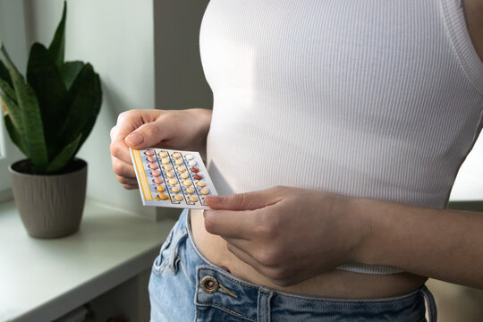 Woman taking birth control pills, holding oral contraceptive blister. Preventing unplanned pregnancy.