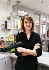 Smiling girl hairdresser with hairdryer in her hands in beauty salon. Selective focus.