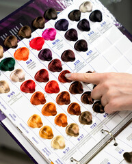 A woman client points to a hair color on a palette with hair dye samples. Close-up. Selective focus.