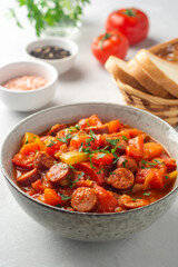 Traditional Hungarian dish Lecho or Lecso or Letscho. Stew with peppers, tomatoes, onions and sausages in bowl on concrete background.