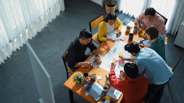 Top down view of diverse people brainstorming and making scrum task board. Group of skilled business team working together and writing sticky notes to share plan and using kanban board. Convocation.