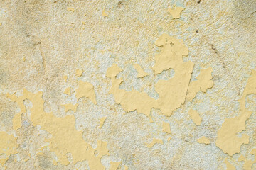 Peeling yellow paint exposes the aged texture of an old wall revealing the underlying surface and its history