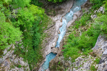 River gorge with clear rushing water amidst verdant greenery and rugged rock formations captured...