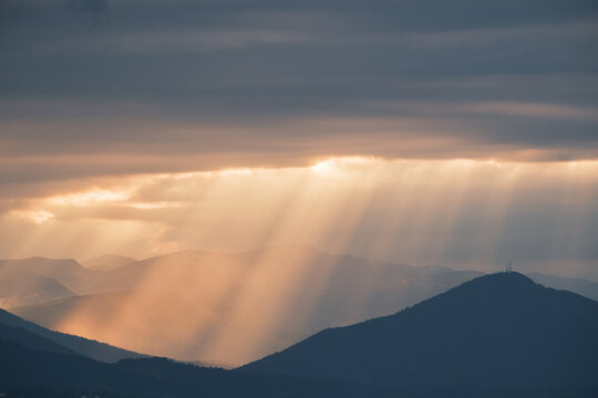 Mountain vista with sunbeams piercing through the clouds creating a serene and dramatic atmosphere
