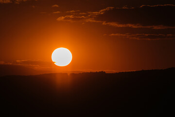 Glowing sun setting over a dark landscape creating a warm and dramatic sky