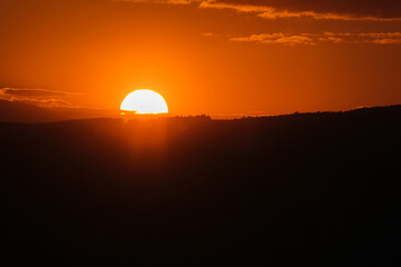 Fiery sunset sinking behind a dark silhouette of hills The sky is orange and the atmosphere is warm
