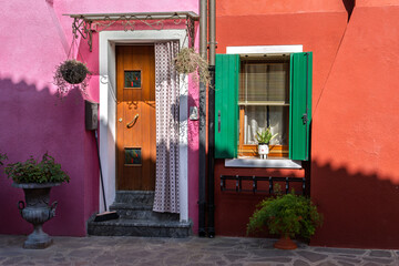 Colorful house entrance with pink and red walls, green shutters, and wooden door in Burano, Italy