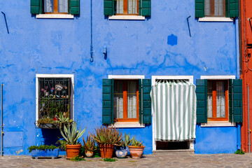 Colorful blue house facade with green shutters and potted plants in Burano, Italy