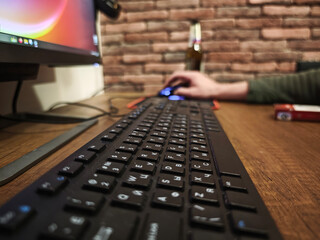Close up of a black keyboard on a wooden desk, with a programmer using a mouse and working on a computer in a home office setting