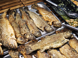 Whole fried trout, ready to eat, are neatly arranged on metal trays at a fish market, offering a delicious and convenient seafood option