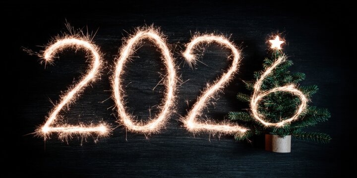 Sparkler shaped as a number glowing on a decorated Christmas tree with colorful ornaments at night.