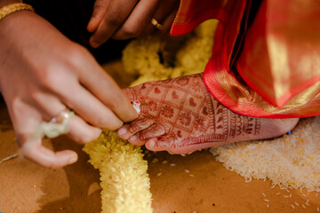 Indian wedding ritual: putting ring on toe during the sacred ceremony. Henna art and traditional...