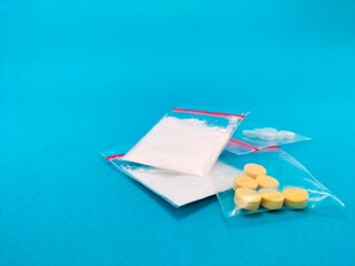 clear plastic bags display various pills and powders drugs on a blue background. 