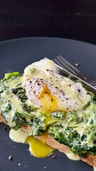 Poached egg on a piece of bread with spinach on the black plate