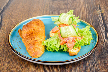 On half of a croissant are ingredients for filling of lettuce leaves, pieces of red fish and cucumbers.