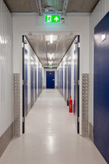 Long hallway within a modern, well-lit self-storage facility with blue doors