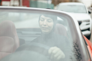A woman, wearing a thoughtful and contemplative expression, is driving a vibrant bright red...
