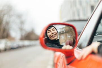 A cheerful woman enjoying herself in a car, reflected in the side mirror, highlighting a delightful...