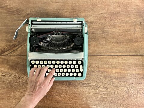 photograph of a typewriter from a zenithal angle, a hand is touching the keys, it is on a wooden table.