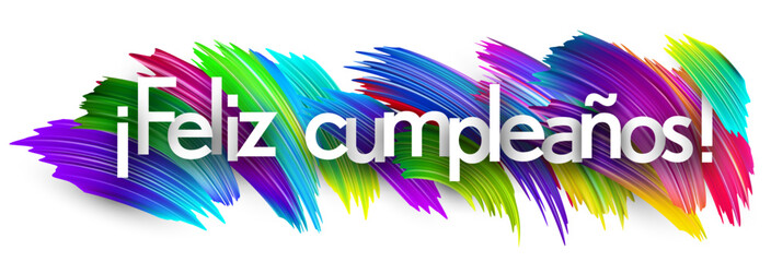 Obraz premium Spanish phrase for Happy Birthday written in white text on colorful paint strokes. Vector illustration.