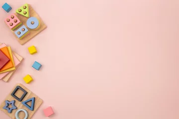 Gordijnen Toy frame on pastel pink background. Natural wooden educational toys and colorful building blocks for children. Top view, flat lay frame © vejaa
