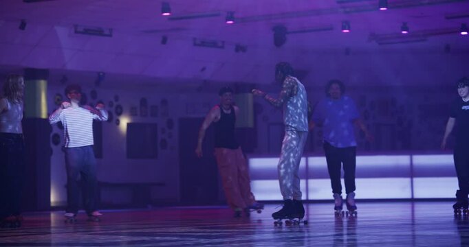Friends cheering on guy roller skating in center of disco room - wide shot