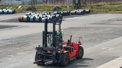 Large red industrial forklift moving steel coils at a port or heavy industry site