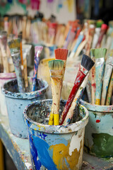 Brushes filled with vibrant colors stand in paint buckets on a artist's workstation during a creative session in a bright studio