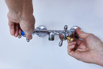 Two hands are loosening worn metal faucet with cross handles, spout is missing from central outlet,...