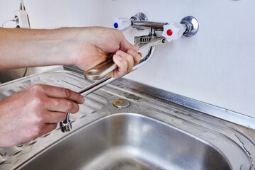 Using adjustable wrench plumber tightens mounting nut of spout on dual handle wall mounted faucet...