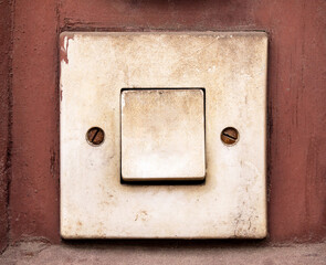 Old dirty electric light switch or doorbell button on a rusty red wall surface, vintage damaged...